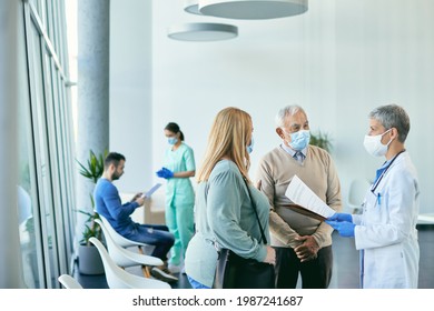 Female doctor and her patients wearing protective face masks while communicating about medical reports in hallway at the hospital. Focus is on senior man. - Powered by Shutterstock