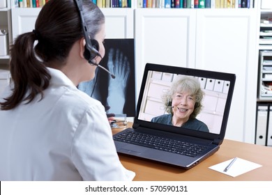 Female Doctor In Her Surgery Office With Headset In Front Of Her Laptop, An X-ray Of A Foot In Hand, Talking With A Senior Patient, Telemedicine Concept