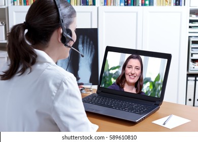 Female Doctor In Her Surgery Office With Headphones In Front Of Her Laptop, An X-ray Of A Foot In Hand, Talking With A Patient, E-health Concept