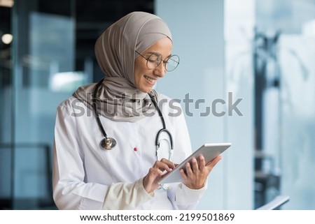 Female doctor in hijab works in modern clinic office, Muslim female doctor uses tablet computer, nurse in medical white coat and glasses with stethoscope.