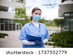 Female doctor holding blue clipboard standing outside hospital or clinic,frontline key medical worker portrait in modern care facility or nursing home complex yard,Coronavirus pandemic outbreak crisis