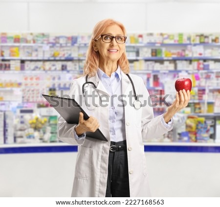 Female doctor holding a clipboard and a red apple inside a pharmacy