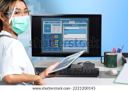 Female doctor holding digital tablet in hand working on electronic medical record with desktop computer then looking back to see something.