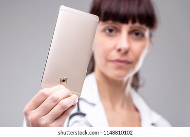 Female Doctor Holding Up A Mobile Phone With The Screen Facing Away From The Viewer And Selective Focus To The Phone In A Close Up View