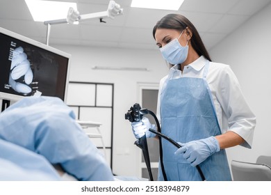 Female doctor holding modern endoscope device before gastroscopy examination. Gastroenterologist with probe to perform colonoscope in white lab coat protective gloves and facial mask - Powered by Shutterstock