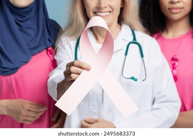 Female doctor holding a pink ribbon for breast cancer awareness, standing with diverse patients, promoting health and solidarity closeup, selective focus. Health care concept - Powered by Shutterstock