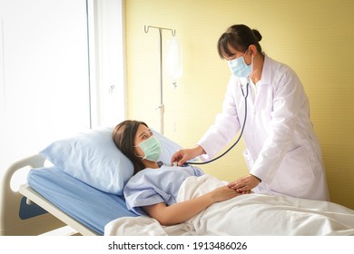 Female Doctor Holding A Stethoscope, Doctor Examining The Heart, Asian Woman Patient Wear A Blue Mask And Lie In A Hospital Bed. Concept Of Medical Service, Health Insurance. Copy Space