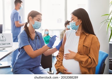 Female Doctor Holding Syringe Making Covid 19 Vaccination Injection Dose In Shoulder Of Pregnant Female Patient, Asian Lady Hug Belly. Flu Vaccine Clinical Trials, Corona Virus Treatment Side Effect