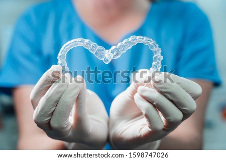Female doctor holding two transparent heart-shaped dental aligners
