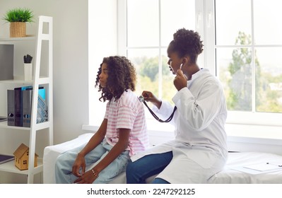 Female doctor listens to back of preteen girl patient to check her lungs, breathing and heartbeat. Doctor listens with stethoscope to African American teenage girl sitting on examination couch. - Powered by Shutterstock