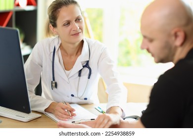 Female doctor listens to her patient while sitting at office desk in medical clinic. Healthcare worker discusses health insurance details with client. - Shutterstock ID 2254938859