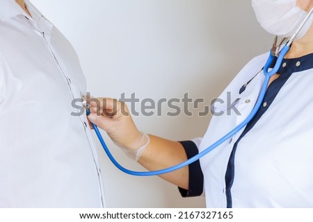 A female doctor listens to the patient's lungs and heart with a phonendoscope on a white background.