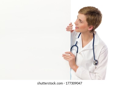 Female Doctor Looking At Banner And Reading. Waist Up Studio Shot Isolated On White.