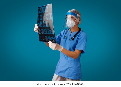 Female Doctor Looking At X-ray Radiographic Or MRI Scan Image. Radiology Specialist In Face Shield, Goggles, White N95 Respirator And Gloves Examining At An Computed Tomography CT, MRI. Healthcare.