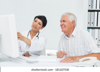 Female Doctor With Male Patient Reading Reports On Computer At Medical Office