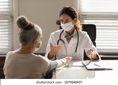 Female doctor in medical facemask measure blood pressure with electronic monitor in hospital. Caring woman GP help examine do checkup of elderly client in clinic. Healthcare, hypertension concept.