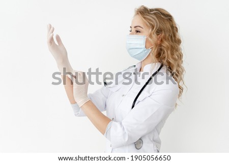 Female doctor in medical uniform and protective face mask wearing surgical gloves, standing with stethoscope against copy space wall in hospital. Concept of healthcare in clinic