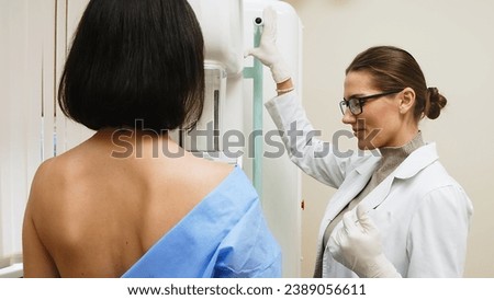 A female doctor in a modern clinic explains the mammography procedure to a topless adult patient undergoing a mammogram. A healthy woman is engaged in cancer prevention in a hospital ward.