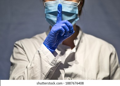 female doctor or nurse with blue medical gloves is wearing a surgical face mask and giving the silence gesture