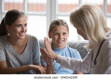 Female Doctor Or Nurse Give High Five To Smiling Small Teen Girl Kid Patient Visit Hospital With Young Mom. Woman GP Pediatrician Show Good Quality Medical Service Cure Little Child Patient At Home.