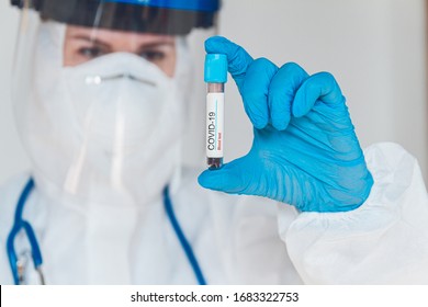 Female Doctor Or Nurse In Protective Suit And Face Shield Holding A Positive Blood Test Result For Coronavirus Or Covid-19.