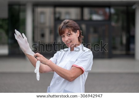 Female doctor or nurse standing outdoors in front of a hospital putting on latex gloves for protection or sterility as she prepares to do an examination