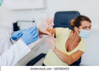 Female Doctor Or Nurse Trying To Give Shot Or Vaccine Against Virus To A Scared Patient. Angry And Distrustful Patient Refuses To Receive It. 