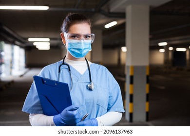 Female Doctor Or Nurse In Uniform Wearing PPE Face Mask Holding Medical Form Clipboard,testing Or Vaccination Drive-thru Facility,portrait Of Serious Rescue Worker During Coronavirus COVID-19 Pandemic