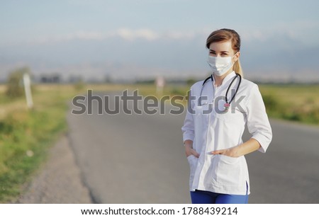 Female doctor or nurse wearing a protective face mask next to a rural road.