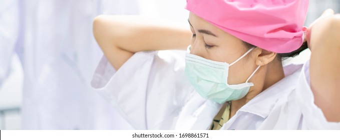 Female Doctor Nurse Wearing And Putting On Protective Gear Of Surgical Mask For Safety, Protection Against Contagious Corona Virus Disease COVID-19, Health Care Worker In Hospital Diagnosing Patients 