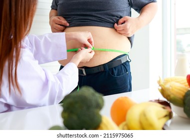 A Female Doctor Or Nutritionist Checks The Health Of An Obese Person Using A Tape Measure Around The Waist Of An Obese Man. Weight Loss Concept. Medical Services In Hospitals.