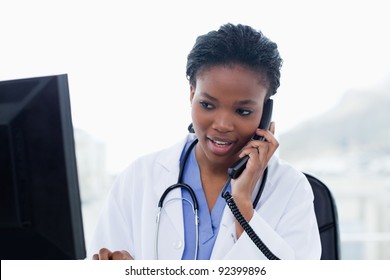 Nainen lääkäri puhelimessa, kun käytät tietokonetta toimistossaan Arkistovalokuva
