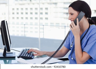 Female doctor on the phone while using a monitor in her office