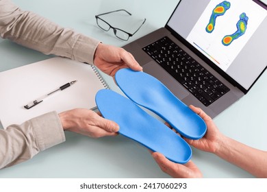 Female doctor orthopedist  presents new custom made insoles to a male patient in a clinic.  Feet recreation and orthotic medicine concept