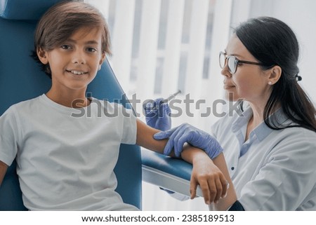 Female doctor pediatrician injecting vaccine to little boy in medical clinic for receiving anti-bodies, immunization boost. Vaccination against coronavirus, hepatitis, flu, measles, chicken pox