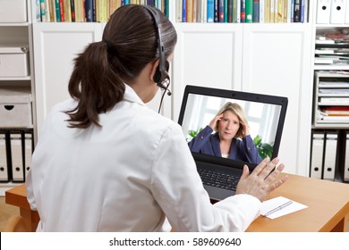 Female doctor or pharmacist in her surgery office with headset in front of her computer talking via video chat with a patient, telling her to take things easy