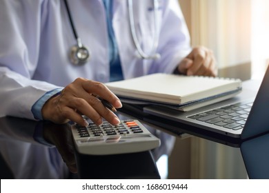Female doctor or physician with stethoscope using calculator and work on computer notebook on the desk at modern office at clinic or hospital. Healthcare costs and fees , Medical finance concept.