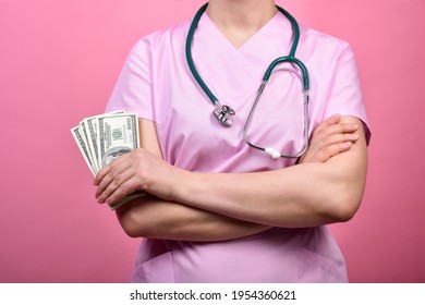 Female doctor in a pink medical scrubs holds dollars in her hands.