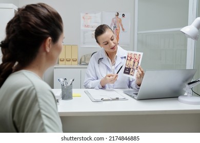 Female Doctor Pointing At Ultrasound Image And Explaining It To Pregnant Woman During Visit