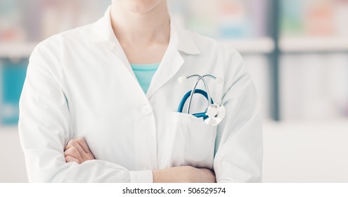 Female doctor posing with arms crossed, stethoscope on foreground, unrecognizable person, healthcare concept