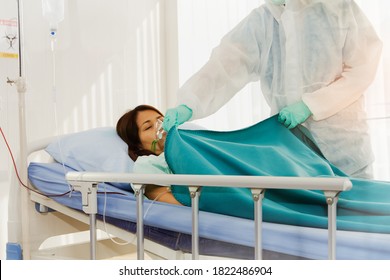 Female Doctor In Protective Clothing Takes Care Of A Woman Who Is Sleeping And Is Infected With Coronavirus (COVID). -19) Incubation In Hospital