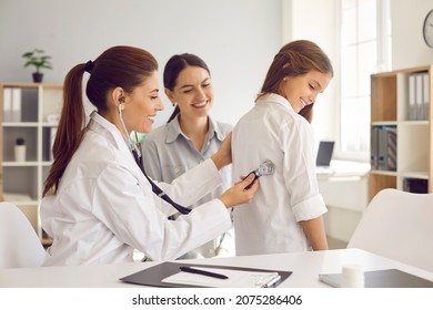 Female doctor puts stethoscope on girl's back and listens to heartbeat and lungs. Pediatrician examines teenage girl in presence of her mother. Concept of health care and pediatric medical examination