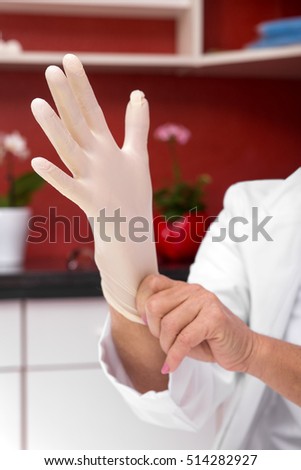 female doctor is putting a latex glove on, office in the background