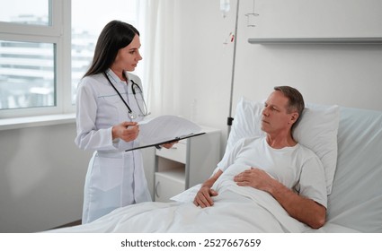 A female doctor reviews medical notes with a male patient resting in a hospital bed. The patient listens attentively while the doctor stands by with a clipboard. The room is bright and professional. - Powered by Shutterstock