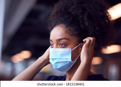 Female Doctor In Scrubs Putting On Face Mask Under Pressure In Busy Hospital During Health Pandemic