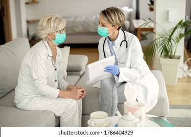 Female Doctor And Senior Woman With Protective Face Masks Talking About Medical Data During A Home Visit. 