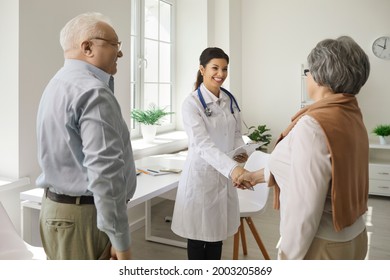 Female doctor shakes hands with an elderly woman who came to the clinic with her husband. Doctor welcomes or congratulates couple of patients on successful recovery. Healthcare concept for seniors. - Powered by Shutterstock