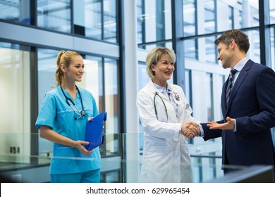 Female doctor shaking hands with businessman in hospital