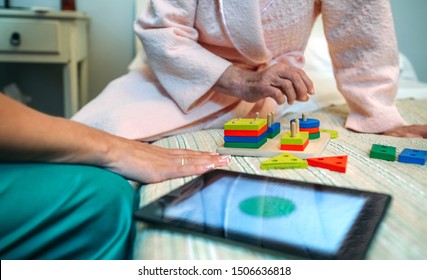 Female Doctor Showing Geometric Shape Game To Elderly Female Patient With Dementia