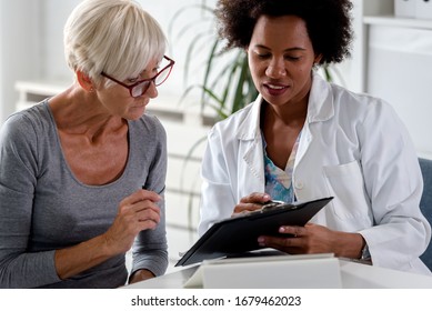 A female doctor sits at her desk and chats to an elderly female patient while looking at her  test results